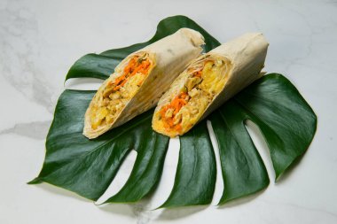 Sebzeli tavuk shawarma dürümü (havuç, salatalık, lahana), ince lavaş ekmeğine sarılmış peynir. Izgara jiroskoplar beyaz mermer arka planda canavar yaprağında servis edilir. sokak yemekleri