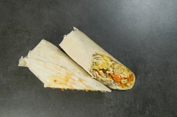 Top view of Chicken meat shawarma isolated on dark stone background. Gyros with carrot, cheese, pickled cucumber, cabbage and French fries wrapped in lavash bread. Grilled halal kebab