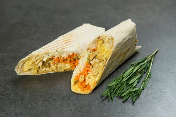 Close-up of Chicken meat shawarma served with fresh rosemary on dark background. Gyros with carrot, cheese, pickled cucumber, cabbage and French fries wrapped in lavash bread. Grilled halal kebab