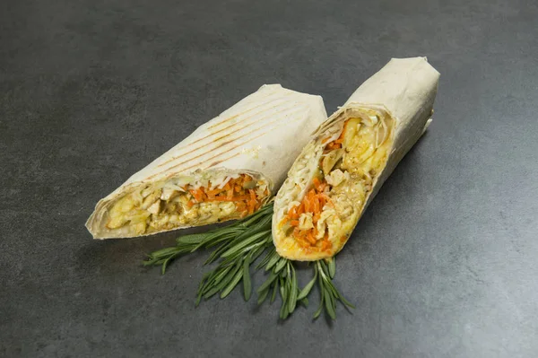 Side view of Chicken meat shawarma served with fresh rosemary on dark background. Gyros with carrot, cheese, pickled cucumber, cabbage and French fries wrapped in lavash bread. Grilled halal kebab