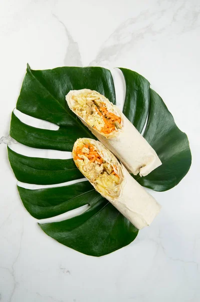 Sebzeli tavuk shawarma rulosunun yukarısından (havuç, salatalık, lahana) ince lavaş ekmeğine sarılmış peynir. Izgara jiroskoplar mermer arka planda canavar yaprağında servis edilir. Doğu sokak yemekleri