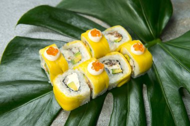 Sağlıklı Japon pirinçsiz suşi rulosunun üzerinde tempura siyah kaplan karidesi (karides) ve havyarla servis edilen havyar (uçan balık yumurtası) taştan arkaplanda egzotik canavar yaprağı.