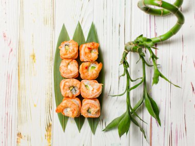 Lezzetli Japon deniz ürünleri suşi rulosu, somon tataki ve bambu yaprakları üzerinde kızarmış siyah kaplan karidesleri. Açık renkli ahşap arka planda, çanağın yanındaki bambu bitkisi.