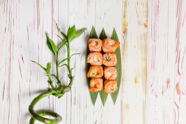 Lezzetli Japon deniz ürünleri suşisinin tam üstünde somon tataki ve bambu yaprakları üzerinde kızarmış siyah kaplan karidesi var. Açık renkli ahşap arka planda, çanağın yanındaki bambu bitkisi.