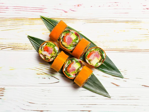 Sağlıklı Japon manzarası bambu yaprakları üzerinde pirinç suşi rulosu servis edilmiyor. Çiğ somon, ton balığı, kaya balığı, avokado, marul, krem peynir havuç dilimlenmiş hafif ahşap zemin