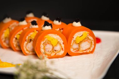 Makro porsiyon saglikli Japon pirinçsiz suşi rulosu. Tempura siyah kaplan karidesi (karides) sarmalanmis. Soslu havyar ve siyah havyarla servis ediliyor. Çiçek, fırça darbesi beyaz tabakta