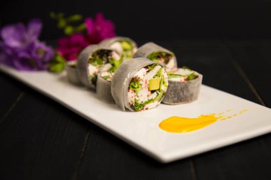 Sağlıklı Japonların yan görüntüsü yengeç eti, avokado, daikon turpuna sarılmış marul ve pirinç suşisi yok. Renkli çiçekler, beyaz tabakta sarı fırça darbesi süslemesi. Siyah arkaplan