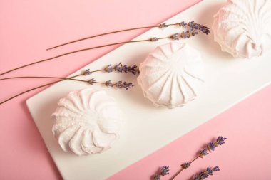 Beyaz tabakta servis edilen üç parça zefir tatlısı ve pastel pembe arka planda kurutulmuş lavanta otları. Rus marşmelovu yumurta beyazı, meyve ezmesi ve organik elma pektin. Seçici Odaklanma