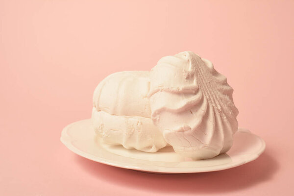 Pieces of souffle airy dessert zefir (zephyr) made of organic pectin and egg whites, similarly to marshmallow and meringue. Served on white plate on pastel apricot background. Copy space image