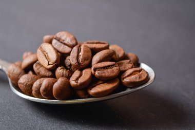 Kavrulmuş kahve çekirdeklerinin makrofotografı koyu arkaplanda gümüş, paslanmaz çelik kaşıkla servis edilir. Yüksek kaliteli organik aroma tohumları. Boşluk metin resmini kopyala