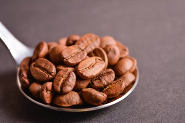 Koyu arkaplanda gümüş, paslanmaz çelik kaşıkla servis edilen kavrulmuş kahve çekirdeklerinin yan görüntüsü. Yüksek kaliteli organik aroma tohumları. Boşluk metin resmini kopyala