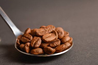 Koyu arkaplanda gümüş, paslanmaz çelik kaşıkla servis edilen kahve çekirdekleri. Yüksek kaliteli organik aroma tohumları. Boşluk metin resmini kopyala