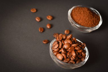 Kavrulmuş kahve çekirdeklerini cam kasede koyu arka planda servis edilen öğütülmüş kahve fincanlarının yan görüntüsü. Yüksek kaliteli organik aroma tohumları. Boşluk metin resmini kopyala
