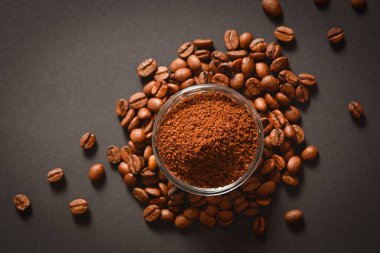 Bir avuç kahve çekirdeğinin üzerinde cam kâsede servis edilen öğütülmüş kahve. Yüksek kalitede organik Arap tohumları. Koyu arkaplana saçılmış kahve çekirdekleri odak dışı. Boşluk metin resmini kopyala