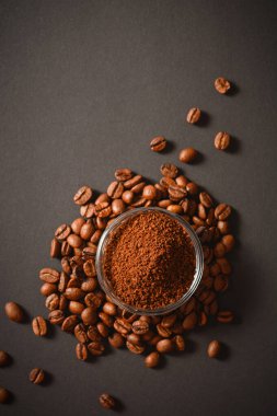 Bir avuç kahve çekirdeğinin üzerinde cam kâsede servis edilen öğütülmüş kahvenin en üst görüntüsü. Yüksek kalitede organik Arap tohumları. Koyu arkaplana saçılmış kahve çekirdekleri odak dışı. Uzay metnini kopyala. Kahve çekirdeği biçimi (siluet) koyu arka planda izole edildi.