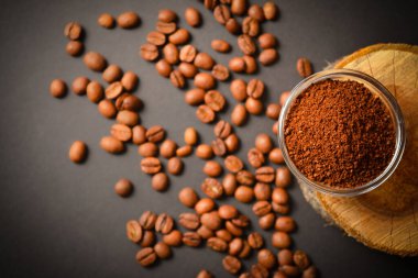 Cam kasede servis edilen öğütülmüş kahvenin üst görüntüsü ahşap kütükte ve dağınık kahveyle. Yüksek kalitede organik Arap tohumları. Koyu arka planda kavrulmuş kahve çekirdekleri odak dışı. Boşluk metin resmini kopyala