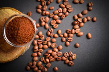 Cam kasede servis edilen öğütülmüş kahvenin tam üstünde, ahşap kütükte, dağınık kahve ile. Yüksek kalitede organik Arap tohumları. Koyu arka planda kavrulmuş kahve çekirdekleri odak dışı. Boşluk metin resmini kopyala