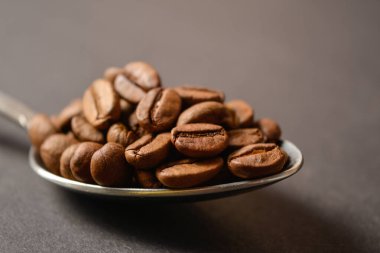 Koyu arkaplanda gümüş, paslanmaz çelik kaşıkla servis edilen kahve çekirdekleri. Yüksek kaliteli organik aroma tohumları. Boşluk metin resmini kopyala