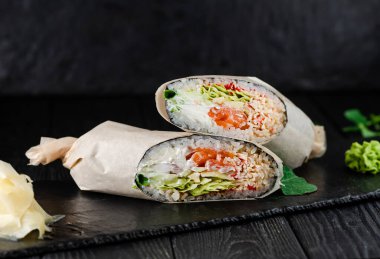 Siyah taş tabakta somon suşi burrito zencefil dilimleri ve wasabi ile servis edilir, ahşap arka plan..