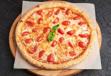 Geleneksel İtalyan dilimlenmemiş domatesli vejetaryen pizza, mozzarella peyniri. Margarita Pizza taze fesleğen yaprağıyla servis edilir. Tahta tahtada kağıt üzerinde tabak. Karanlık arka plan. Kırsal Gıda