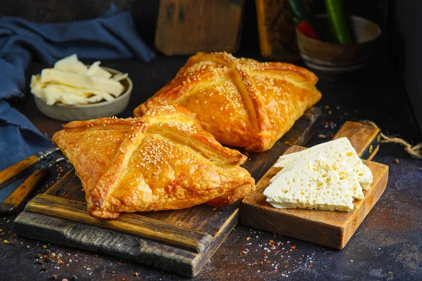 Khachapuri, tahtanın üzerinde servis edilen peynirle koyu arka plandaki malzemelerin yanında dağınık baharatlarla servis ediliyor..