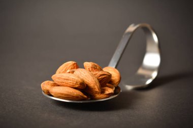 Gümüş metal paslanmaz çelik kaşıkta servis edilen yakın plan badem fıstığı. Karanlık arka planda badem. Yaratıcı gıda konsepti. Çiğ fındık. Uzay resmini kopyala. Tek bir nesne. Mutfak hala hayat dolu