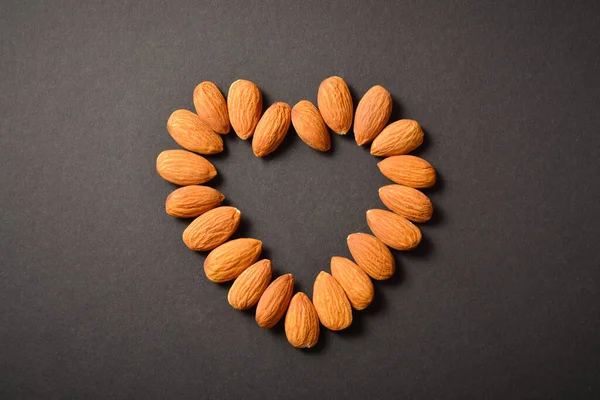 Karanlık arka planda badem kalp siluetinin yatay görüntüsü. Kalbin çiğ fındık şeklinin üst görüntüsü. Yaratıcı gıda konsepti. Çiğ fındık. Uzay resmini kopyala. Tek bir nesne. Mutfak hala hayat dolu