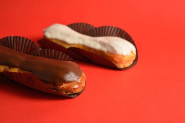 Klasik Fransız tatlılarının yan görünüşü. Kremayla dolu beyaz ve siyah çikolatalı ekler tatlı kağıdında servis ediliyor. Kırmızı arka planda iki Puffy Eclair. Choux hamur işi. Boşluk resmini kopyala