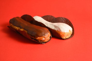 Klasik Fransız tatlıları işte. Biri beyaz çikolatalı, diğeri kremayla dolu koyu çikolatalı, kırmızı arka planda servis ediliyor. Yan görüş. Boşluk resmini kopyala