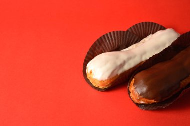 Klasik Fransız tatlıları işte. Biri beyaz çikolatalı, diğeri kremayla dolu koyu çikolatalı, kırmızı arka planda servis ediliyor. Yan görüş. Boşluk resmini kopyala