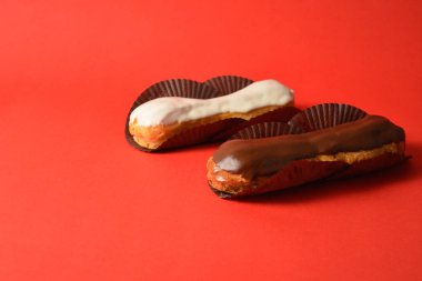 Klasik Fransız tatlıları işte. Biri beyaz çikolatalı, diğeri kremayla dolu koyu çikolatalı, kırmızı arka planda servis ediliyor. Yan görüş. Boşluk resmini kopyala