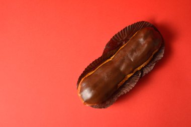 Klasik Fransız tatlısının en iyi manzarası. Kremayla doldurulmuş kremalı siyah çikolatalı ekler tatlı kağıdında servis ediliyor. Kırmızı arka planda Puffy Eclair. Choux hamur işi. Boşluk resmini kopyala