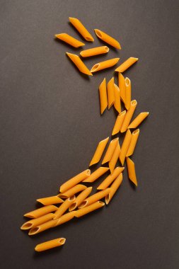 Raw durum buğday makarnasının dikey görüntüsü. Geleneksel İtalyan makarnası. Koyu arkaplanda pişmemiş makarna. Dağılmış makarna Yemek konsepti. Yakın çekim buğday şekli. Mutfak hala hayat dolu