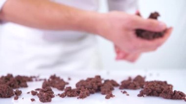 Pasta şefi beyaz bir masaya çikolata parçacıkları atıyor. Çikolata yavaş çekimde beyaz arka plana düşer. Birisi tatlı yapıyor..
