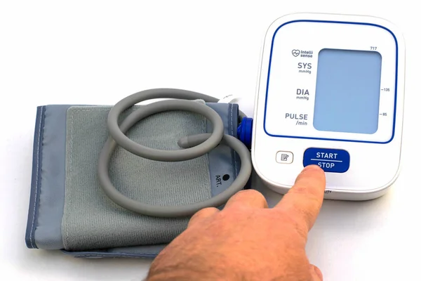Das Gerät zur Messung des Blutdrucks Tonometer befindet sich auf weißem Hintergrund die Person drückt den Startknopf mit dem Finger — Stockfoto