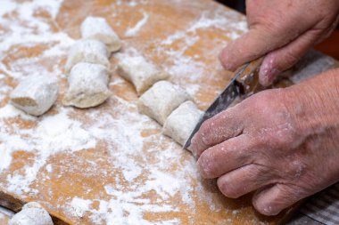 Bir kadın elleriyle tahta kesme tahtasına hamur tatlısı yapar.