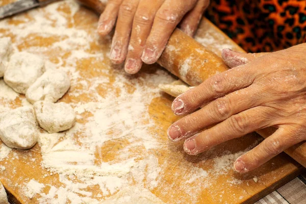 A woman makes dumplings with her hands on a wooden cutting Board rolls out the dough with a wooden rolling pin — Stock Photo, Image