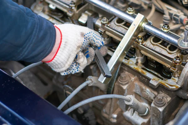 O mecânico ajusta a folga no mecanismo de válvula do motor do carro com a ajuda de dipsticks — Fotografia de Stock