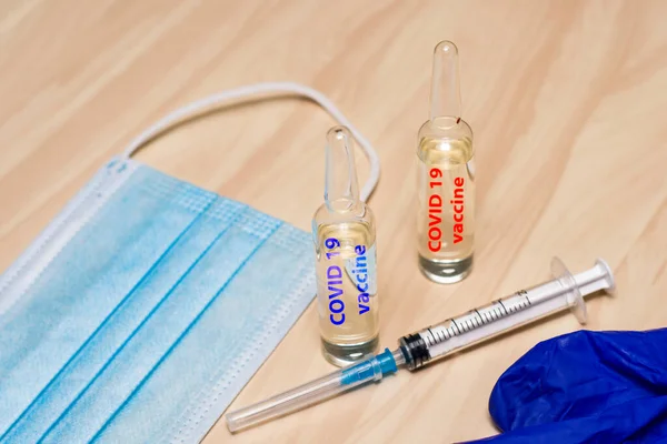 a syringe mask gloves and ampoules labeled covid19 vaccine in blue and red are on the table. High quality photo
