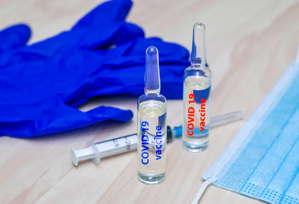 a syringe mask gloves and ampoules labeled covid19 vaccine in blue and red are on the table. High quality photo