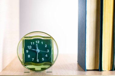 Saat rafta, kitap yığınının yanında.