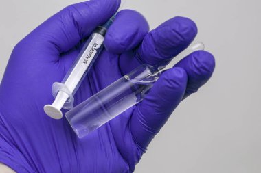 Mavi tıbbi eldivenli bir elin içinde bir şırınga ve bir ampul ilaç var. Yüksek kalite fotoğraf