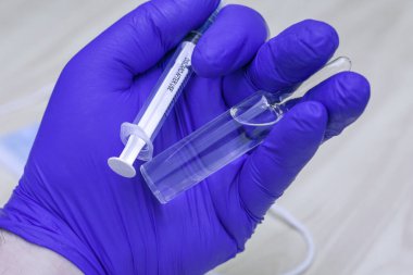 Mavi tıbbi eldivenli bir elin içinde bir şırınga ve bir ampul ilaç var. Yüksek kalite fotoğraf