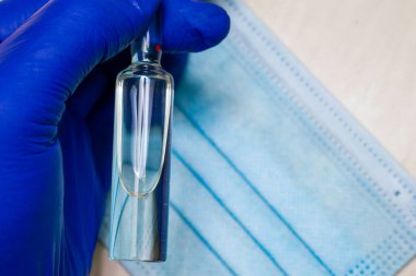 Tıbbi bir eldivenin içindeki bir el tıbbi bir maskenin arka planına karşı bir ampul ilaç tutar. Yüksek kalite fotoğraf