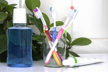 Cam bardakta beş diş fırçası gargara ve banyo masasının üzerinde yeşil yaprakların olduğu bir tüp diş macunu. Yüksek kalite fotoğraf