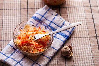 Sarımsağın yanındaki peçetede cam bir tabakta lahana turşusu. Lahanaya saplanmış metal bir çatal.