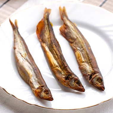 Beyaz bir tabakta tütsülenmiş üç kapelin. Yüksek kalite fotoğraf