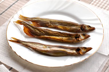 Beyaz bir tabakta tütsülenmiş üç kapelin. Yüksek kalite fotoğraf