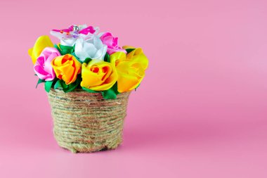 El yapımı yapay gül buketi. Kumaş kurdeleden yapılmış. Arka planda pembe kartpostal arka planında eski bir tencerede.