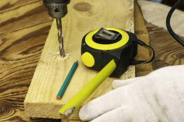 Tahtada elektrikli matkapla bir tahta delen bir adam var. Bir mezura ve kalem konsepti tamiri var. Yüksek kalite fotoğraf